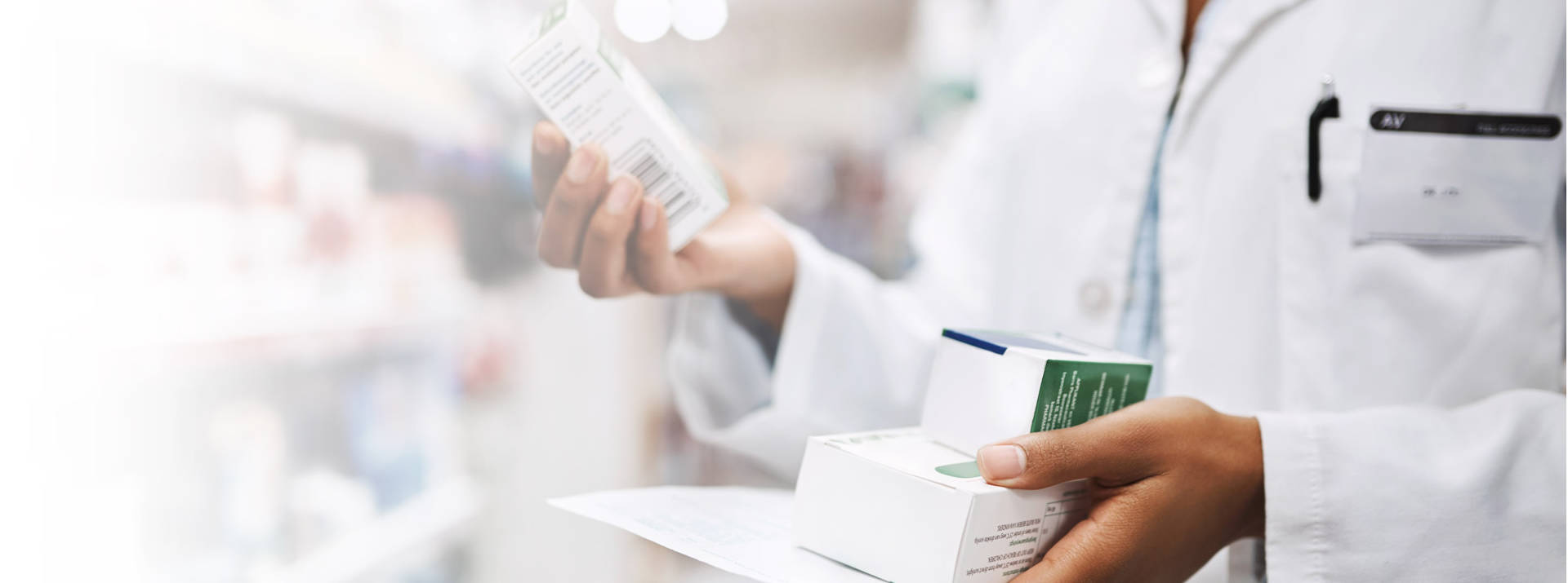 Pharmacist in white coat holding two medicine boxes in one hand and one medicine box in other